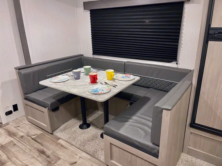 RV rental dinette: U-shaped booth seating, a table with place settings, and a black window blind for privacy.. Coleman Lantern 2022