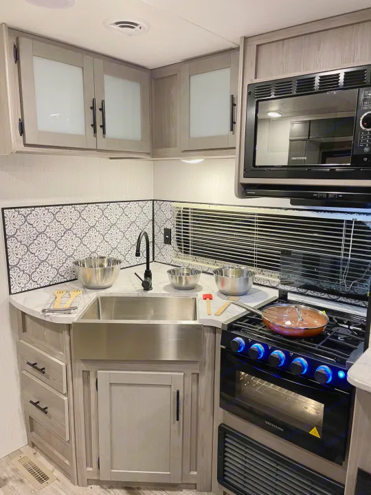Sleek RV rental kitchen with a stainless steel sink, black stove, microwave, and decorative backsplash for comfortable travel.. Coleman Lantern 2022
