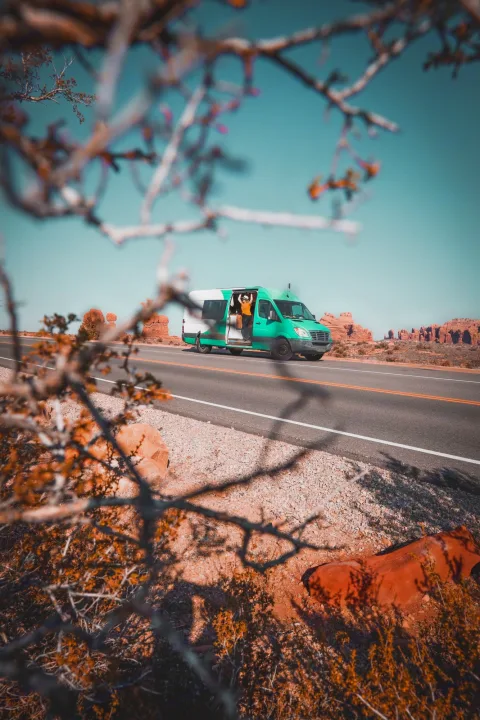 A vibrant green camper van, side door open with person inside, parked on a desert road with red rock formations.. Mercedes-Benz sprinter 2008