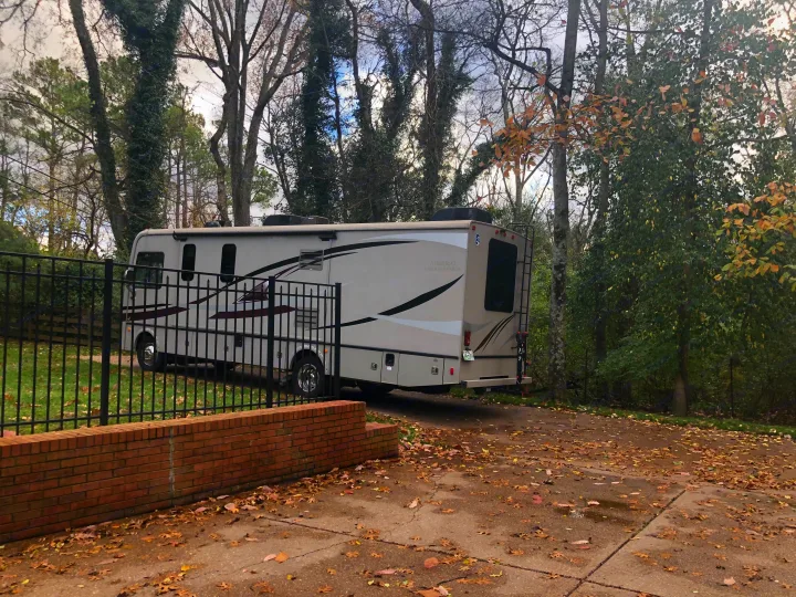 Admiral RV rental, a beige motorhome, parked on a leaf-strewn driveway. Tall trees and a fence define the autumn outdoor scene.. Forest River Other 2021