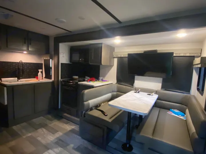 Spacious rv rental interior showing a dark kitchen with backsplash and a comfortable U-shaped dinette lounge.. Forest River Other 2021