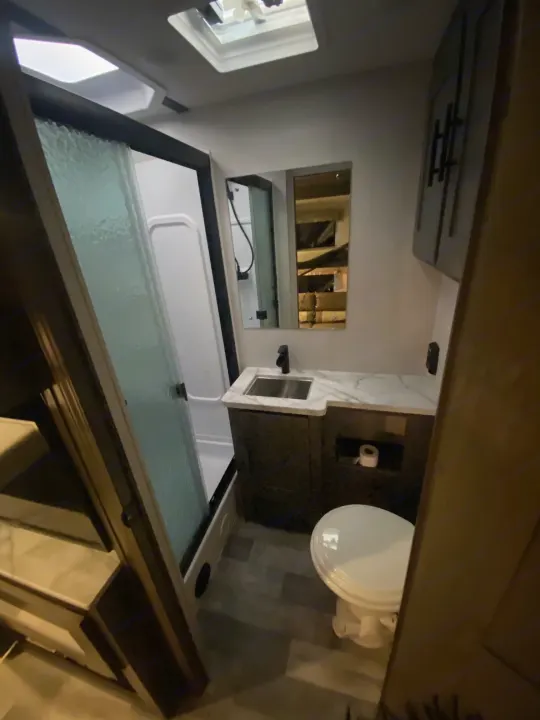 This RV rental features a compact bathroom with a white toilet, vanity, and a shower with a glass enclosure.. Forest River Other 2021