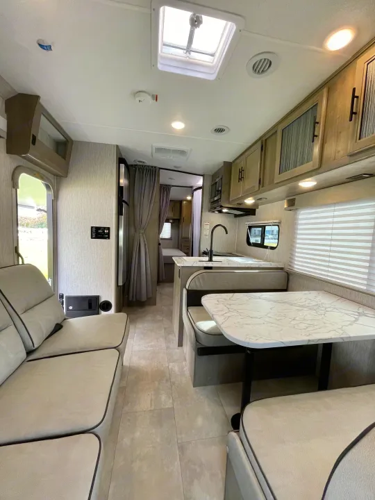 Spacious RV rental interior with a modern kitchen, dining booth, and sofa seating, offering comfort and style.. Coachmen Freelander 2021
