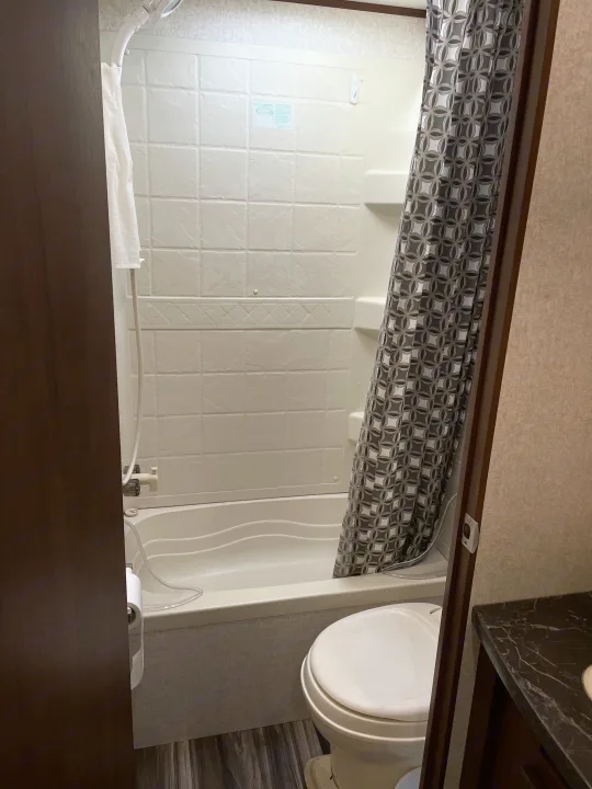 RV rental bathroom features a white tub/shower combo, toilet, and dark patterned curtain. Clean, compact design.. Jayco Jay Flight SLX 2017