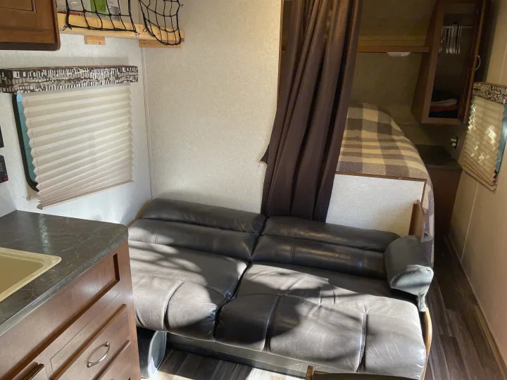 RV rental's inviting interior: leather sofa, kitchen area, and private sleeping nook behind a curtain.. Jayco Jay Flight SLX 2017