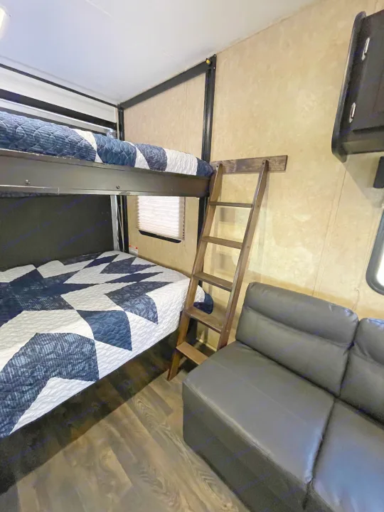 This RV rental interior features cozy bunk beds with bedding, a ladder, and a black sofa, maximizing sleeping and seating space.. Dune Sport Toy Hauler 2017