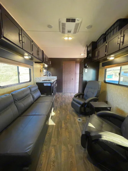 Spacious rv rental interior featuring a leather couch, kitchenette, two recliners, and wood floors.. Dune Sport Toy Hauler 2017