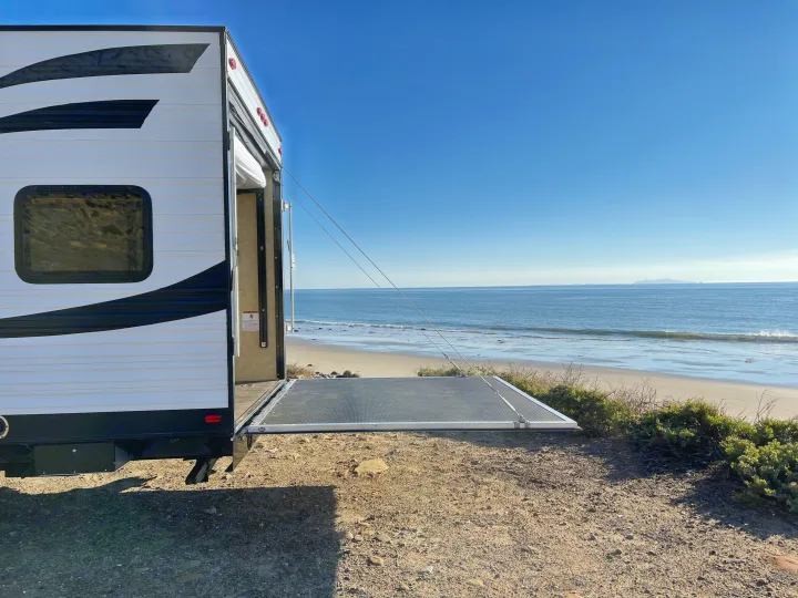 RV rental parked at the beach with its back ramp open, creating a patio overlooking the ocean and sandy shore.. Dune Sport Toy Hauler 2017