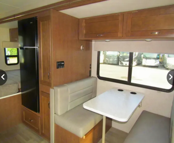 Discover this cozy RV rental interior, showcasing a practical dinette, refrigerator, and bed, ideal for your next trip.. Winnebago Vita 2019