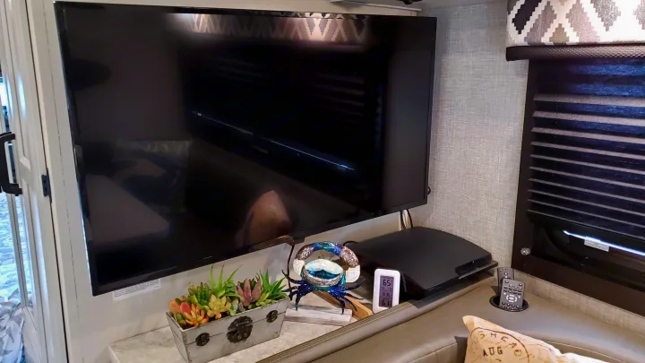 Inside an RV rental, featuring a TV, gaming console, remotes, and cozy decor with succulents.. Jayco Redhawk 2022