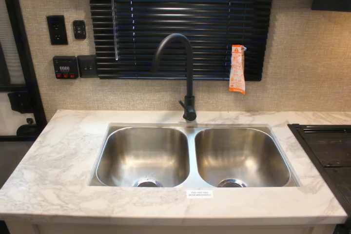 RV rental kitchen: a clean double sink, modern black faucet, and marble-look counter. Controls and stovetop are visible, indicating this unit is winterized.. Jayco Jay Flight SLX 224BH 2022