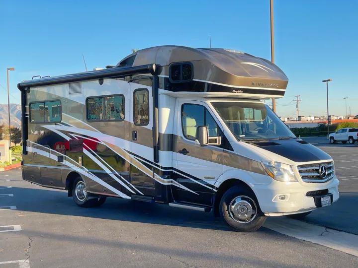 Two-tone Winnebago Navion rv rental, built on a Mercedes-Benz chassis, parked outdoors under a clear sky.. Itasca Navion 2016