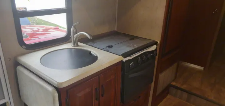 Compact RV rental kitchen features a covered sink, stove, and oven. Wooden cabinetry and practical layout for travel.. Forest River Forester 2017