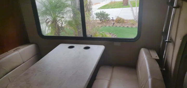 Inside this RV rental: a cozy dinette with tan seats, table & cupholders, plus a window view of palm trees and a lawn.. Forest River Forester 2017