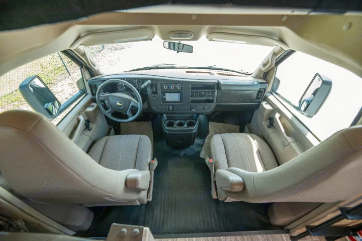 Front cabin of an RV rental: driver & passenger seats, dashboard, steering wheel, and central console.. Forester LE 2018