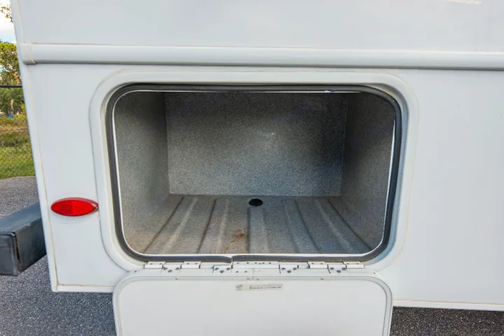 RV rental: Empty, open side storage compartment on a white RV, showing textured interior and a drain hole.. Forester LE 2018