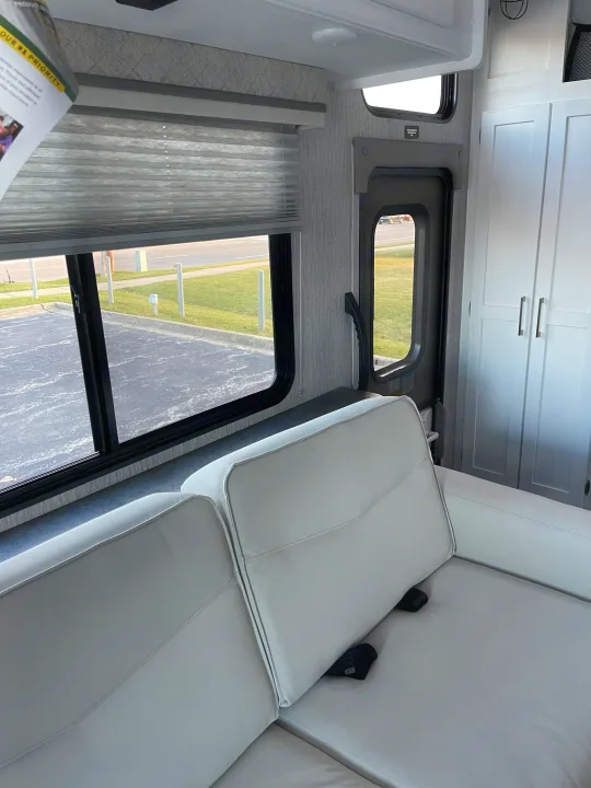 RV rental interior: Comfortable seating, a window with blinds, and white storage cabinets are visible, ready for travel.. Forest River Coachmen Pursuit 2022