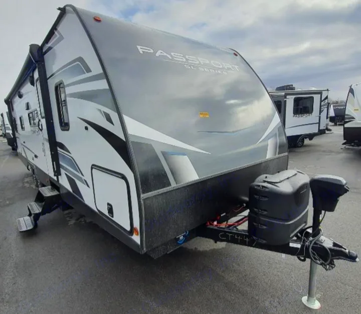 This sleek grey and white Passport travel trailer, ideal for rv rental, features an awning, steps, and propane tanks, ready for adventure.. Keystone RV Passport SL 2022