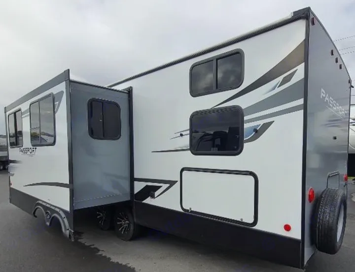 A white and gray Passport travel trailer RV rental, with its slide-out extended, perfect for road trips.. Keystone RV Passport SL 2022