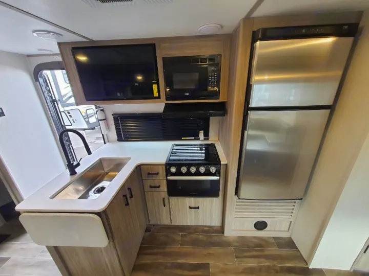 This rv rental boasts a compact yet full-featured kitchen with a sink, stove, microwave, fridge, and wall-mounted TV.. Keystone RV Passport SL 2022