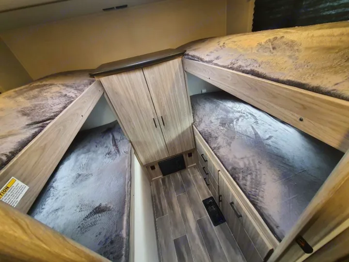 RV rental bunk beds offer comfy, stacked sleeping. Four bunks with soft grey blankets & central storage for a family.. Keystone RV Passport SL 2022