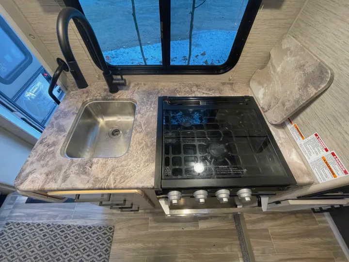 Compact RV rental kitchen featuring a sink, black stove, and patterned countertop. Ideal for camper cooking.. Thor Four Winds 2021