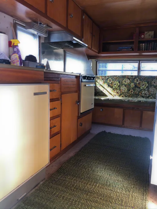 Explore a charming vintage RV rental interior! Features a retro kitchen with wood cabinets, floral dinette, and sunlit living space.. Holiday Rambler Traveler 1964