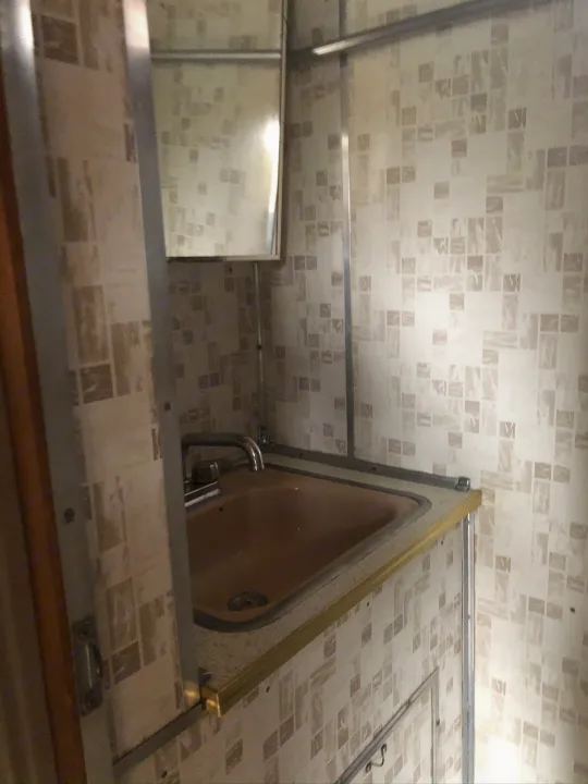 Compact RV rental bathroom with a tan sink, chrome faucet, mirror, and patterned walls.. Holiday Rambler Traveler 1964