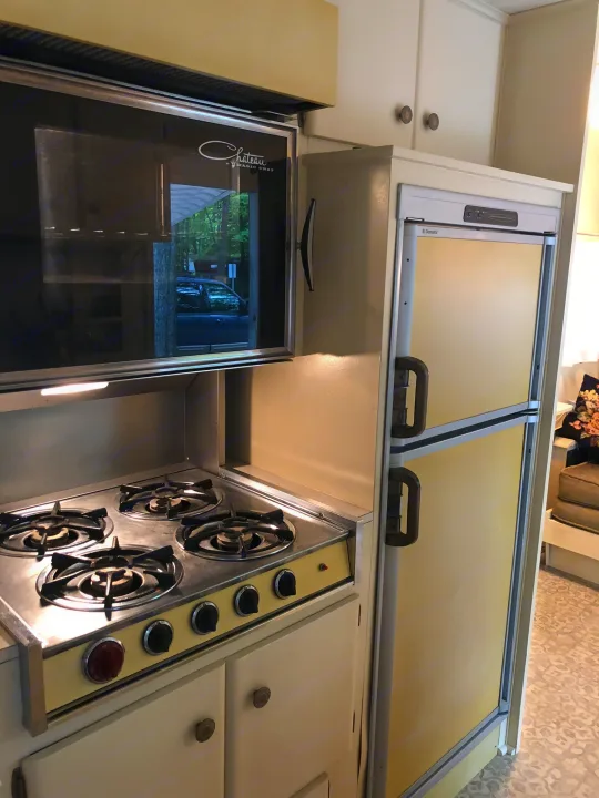 Compact RV rental kitchen featuring a microwave, stove, and a vintage-style refrigerator.. Holiday Rambler Vacationer 1969
