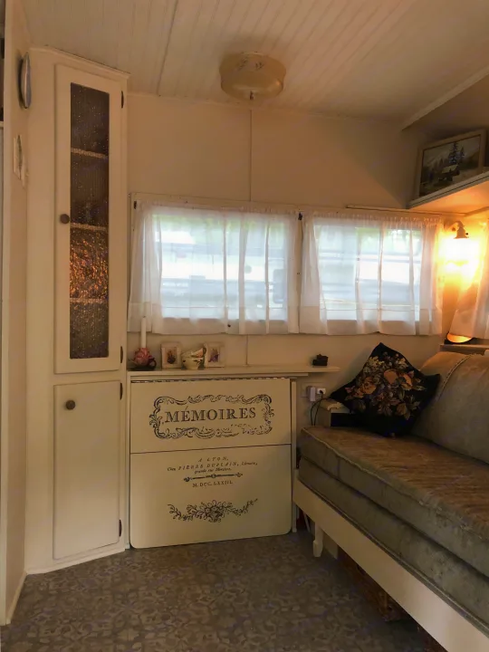 An inviting RV rental interior with vintage French decor, including custom 'Mémoires' cabinetry and a comfortable sofa.. Holiday Rambler Vacationer 1969