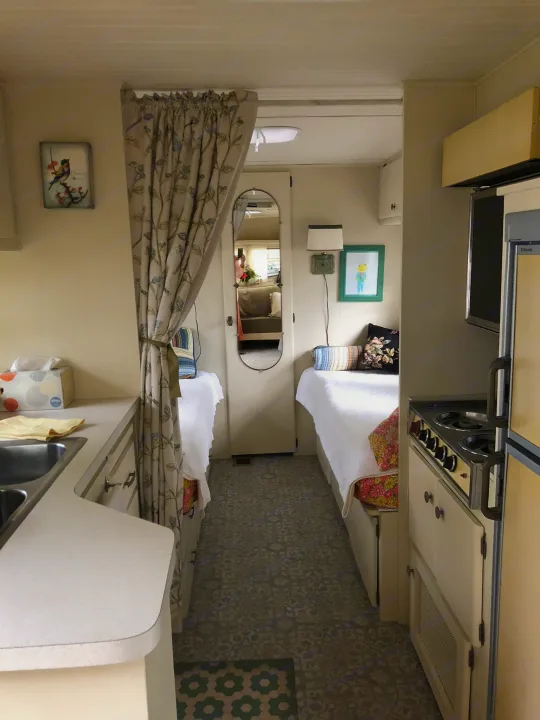 A cozy RV rental interior, featuring a compact kitchenette on the left and twin-style beds on either side of the narrow hall.. Holiday Rambler Vacationer 1969