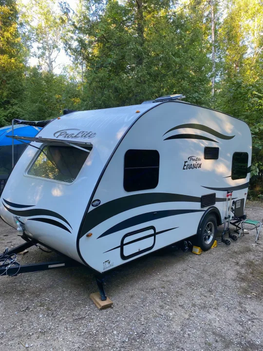 A ProLite Evasion travel trailer, an RV rental, is set up in a lush wooded campsite.. ROULOTTE PROLITE ROULOTTE PROLITE 2020
