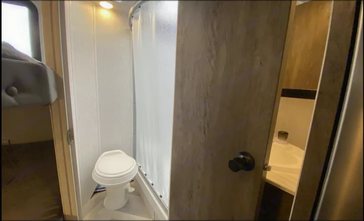 Compact RV rental bathroom with toilet and shower, plus a peek at the sink and sleeping area for your travels.. Forest River Salem Cruise Lite 2022