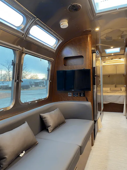 Spacious Airstream RV rental interior, showing a modern living area with couch, TV, and view into the cozy bedroom.. Airstream Globetrotter 2022