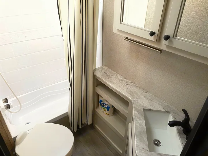 Modern RV rental bathroom featuring a white tub/shower, toilet, and a sleek grey vanity with a white sink & black faucet.. Highland Ridge Mesa Ridge 2021