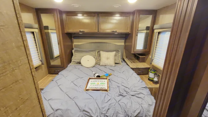 Cozy RV rental bedroom with dark wood cabinets, a queen bed, and camping-themed decor. Perfect for your next adventure.. Thor A.C.E. 2018