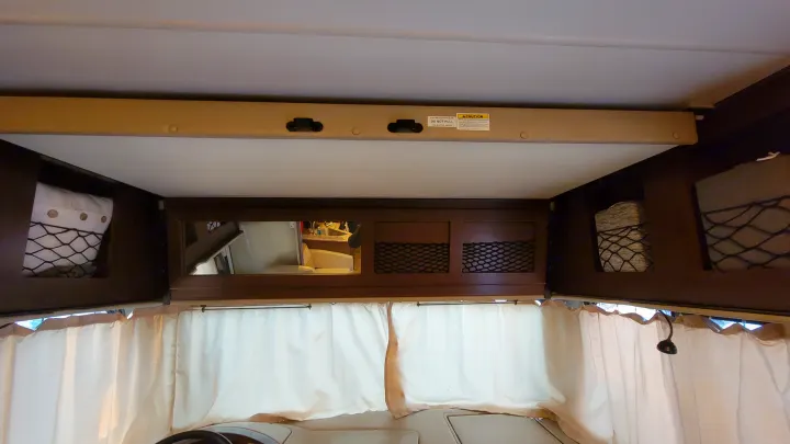 RV rental interior showing an overhead bed/bunk, storage nets, and curtains, highlighting a compact living area.. Thor A.C.E. 2018