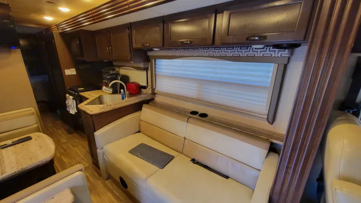 Inside this clean RV rental: kitchen with sink, stovetop, microwave; light wood floors, comfy light-colored seating.. Thor A.C.E. 2018