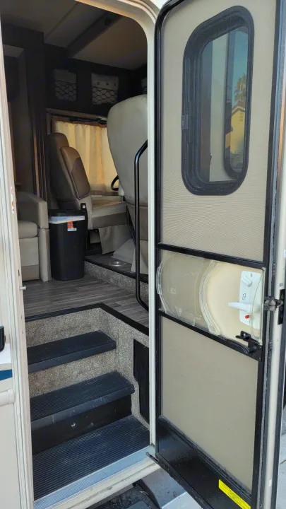 Interior view of an RV rental looking in from the open door, showing entrance steps, a door window, and the living space.. Thor A.C.E. 2018