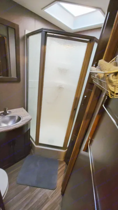 Compact RV rental bathroom interior featuring a frosted shower, small sink, wood-look flooring, and a bright skylight.. Thor A.C.E. 2018