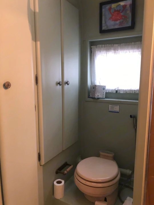 RV rental bathroom features a compact composting toilet, window, cabinetry, and a charming crab picture.. Holiday Rambler Vacationer 1969