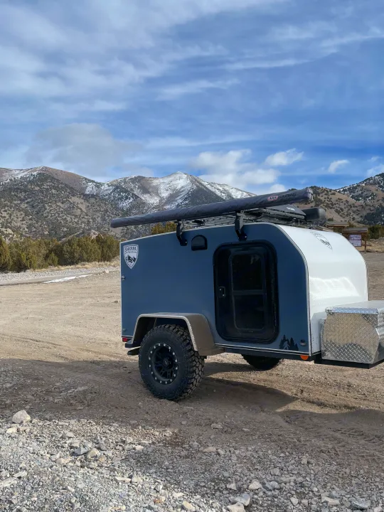 Rugged teardrop camper, ideal for an RV rental mountain adventure. Ready for off-grid exploration in the snow-capped terrain.. Sherpa trailers Big foot 2022