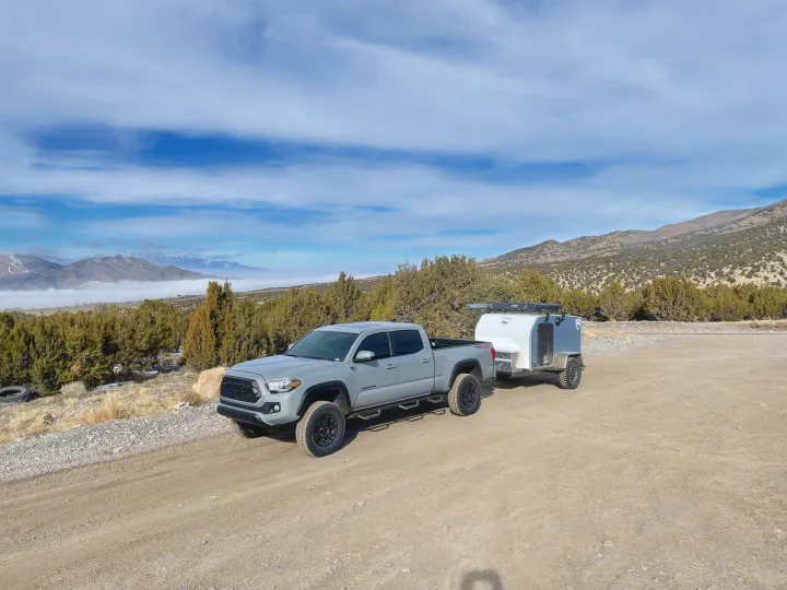 Grey Toyota Tacoma truck towing an overland camper on a dirt road. Mountains & fog in background. Perfect RV rental setup!. Sherpa trailers Big foot 2022