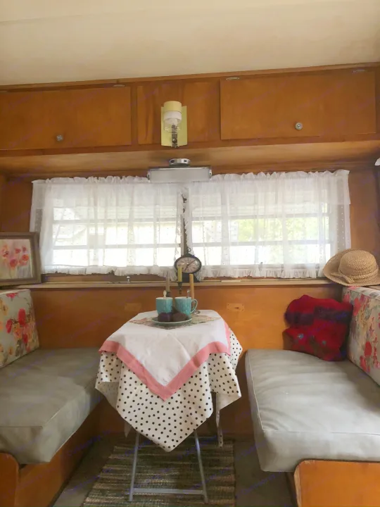 Cozy vintage camper RV rental interior, featuring a quaint table set for tea and comfy bench seating.. Holiday Rambler Traveler 1965