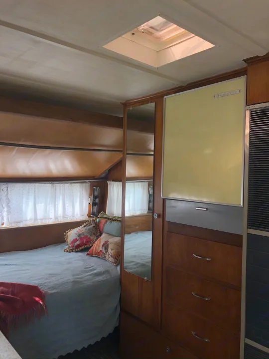 Cozy RV rental bedroom with wood paneling, a bed, Dometic fridge, ceiling skylight, and AC unit.. Holiday Rambler Traveler 1965
