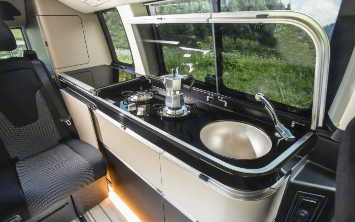 Modern RV rental interior: Compact kitchen with stove, sink, moka pot, and large window with scenic outdoor view.. Mercedes Marco Polo 2022