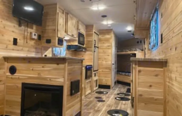 Inside a cozy ice fishing RV rental: rustic wood walls, kitchen, fireplace, TV, bunks, and floor holes for ice fishing.. Glacier Ice House Glacier Ice House Trailer 2019