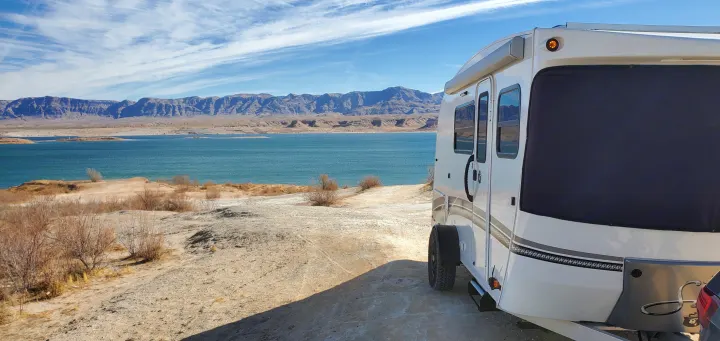 Experience an RV rental: a white trailer parked lakeside, offering stunning views of a vast blue lake and distant mountains.. InTech RV Sol Horizon 2020