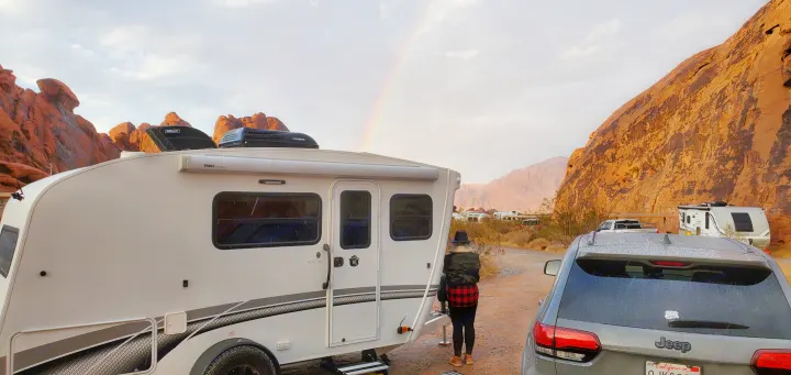 An RV rental travel trailer and Jeep at a stunning red rock campsite with a person and a vibrant rainbow overhead.. InTech RV Sol Horizon 2020