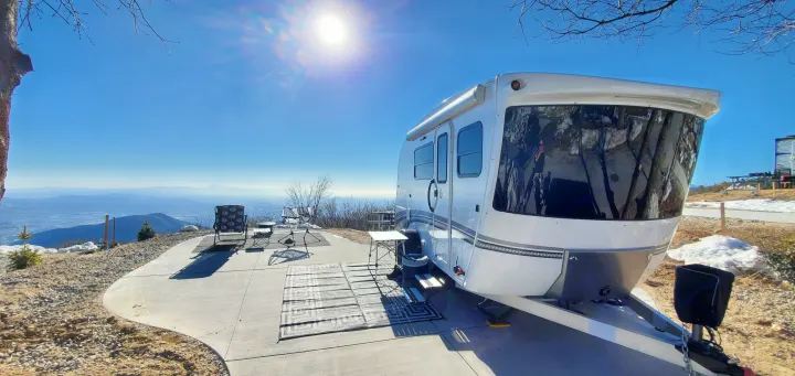 Stunning RV rental mountain view: white camper on concrete pad with chairs & valley vista under clear skies.. InTech RV Sol Horizon 2020